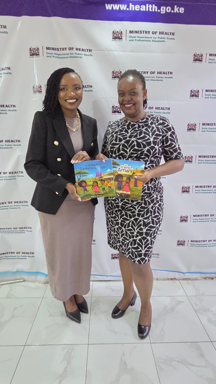 Dr Phyllis Kimani and a colleague hold copies of My Friend Amani and Siku Kishada cha Zumbarau Kilipopaa at the Ministry of Health.