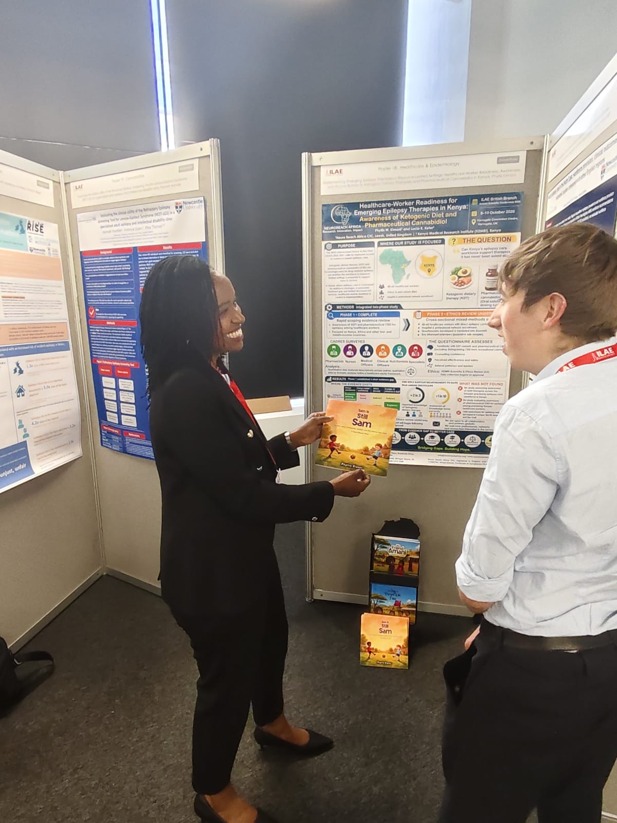 Phyllis showing the NeuroReach Friends Series books to a visitor at her poster